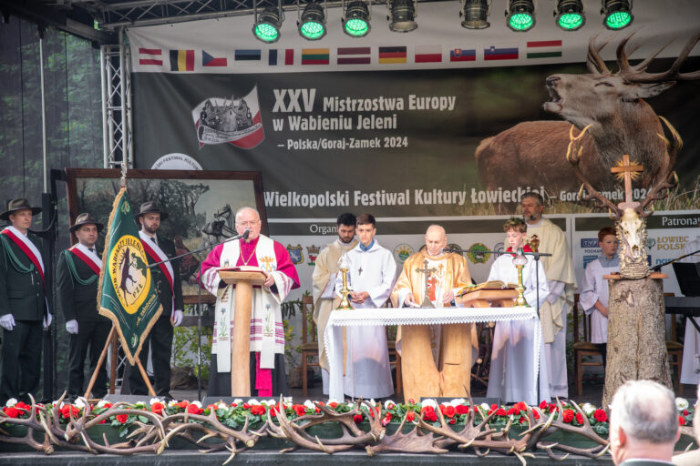 Geistliche feiern die Hubertusmesse vor einem Hirschplakat bei der Hirschruf-EM 2024 in Polen