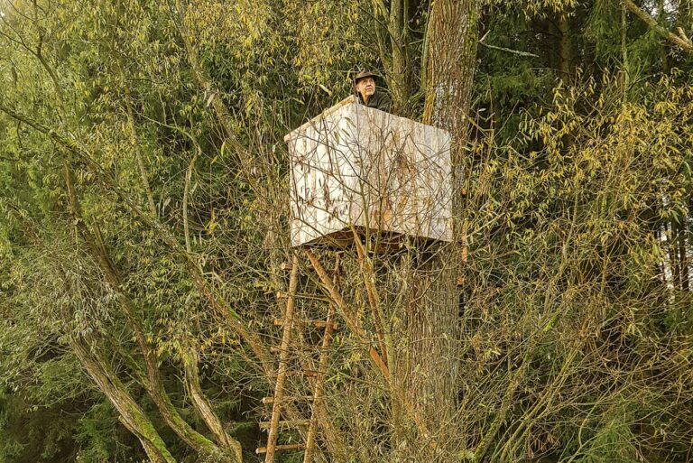 Jäger auf einem Hochstand in einem Baum für optimale Tarnung im Jagdrevier.