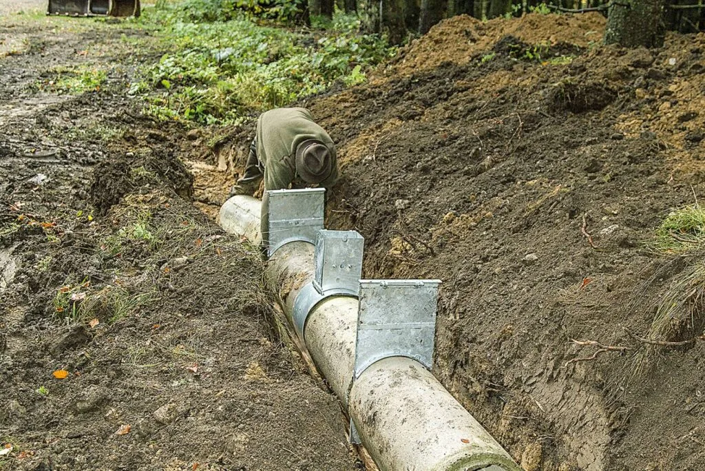 Jäger baut eine künstliche Fuchsröhre aus Holzstämmen und Metallblechen in einen Erdgraben im Wald