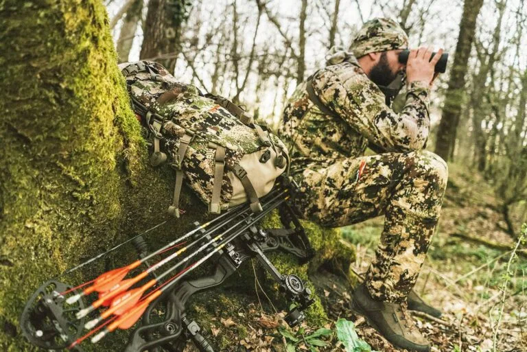 Bogenschütze in Tarnkleidung beobachtet aufmerksam das Gelände, während sein Bogen bereit für den Einsatz ist.