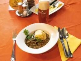 Traditionelles Rehbeuschel mit Semmelknödel, serviert auf einem gedeckten Tisch mit Bier.