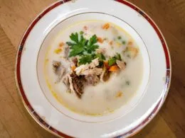 Fasanensuppe serviert in einer klassischen Porzellantasse mit frischem Gemüse und Kräutern