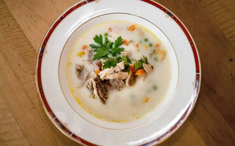 Fasanensuppe serviert in einer klassischen Porzellantasse mit frischem Gemüse und Kräutern