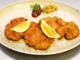 Knuspriges Rehschnitzel mit Zitronenscheiben und Beilagen auf rustikalem Teller – Wildbret-Genuss vom Rehschlögel.