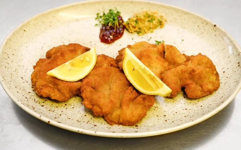 Knuspriges Rehschnitzel mit Zitronenscheiben und Beilagen auf rustikalem Teller – Wildbret-Genuss vom Rehschlögel.