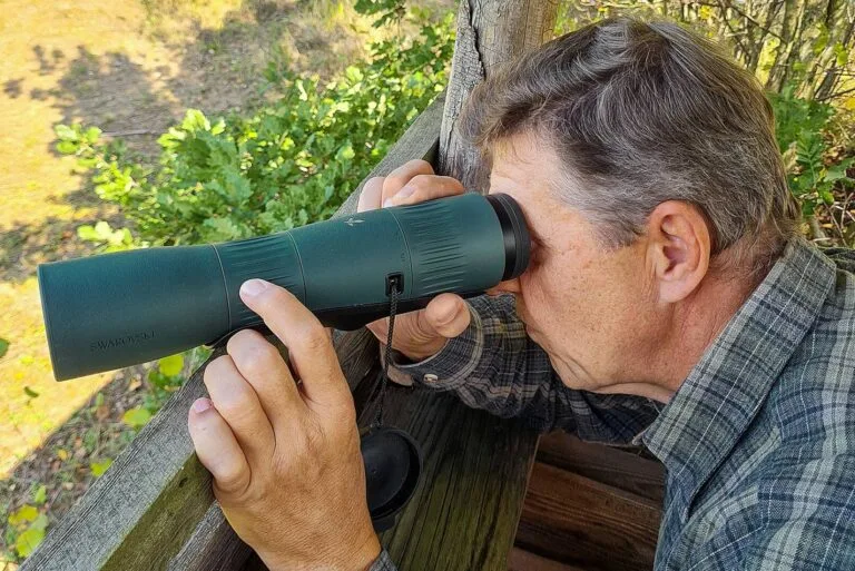 Jäger oder Naturbeobachter nutzt ein grünes Spektiv auf einem Hochsitz zur Wild- oder Landschaftsbeobachtung