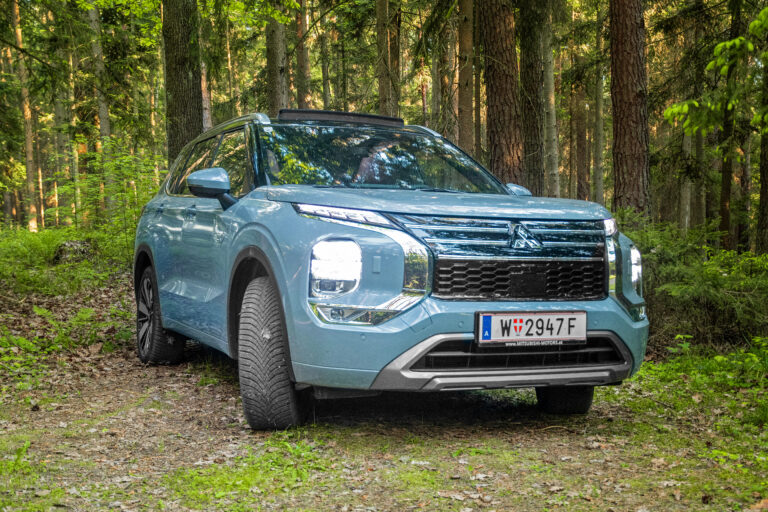 Mitsubishi Outlander PHEV frontal im Wald, mit eingeschaltetem Licht