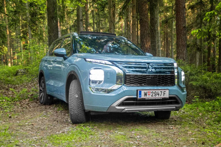 Mitsubishi Outlander PHEV frontal im Wald, mit eingeschaltetem Licht