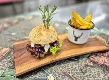 Saftiger Wild-Burger mit Rotkraut, Schnittlauchsauce und Rosmarin-Garnitur, serviert mit knusprigen Potato Wedges im Emaille-Becher