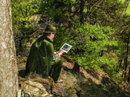 Jägerin in traditioneller Kleidung nutzt ein Tablet im Wald zur digitalen Revierbeobachtung