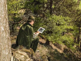 Jägerin in traditioneller Kleidung nutzt ein Tablet im Wald zur digitalen Revierbeobachtung