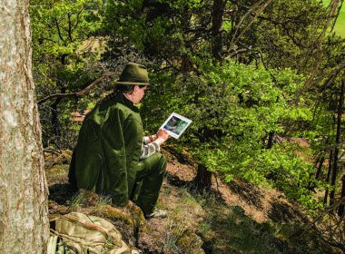 Jägerin in traditioneller Kleidung nutzt ein Tablet im Wald zur digitalen Revierbeobachtung