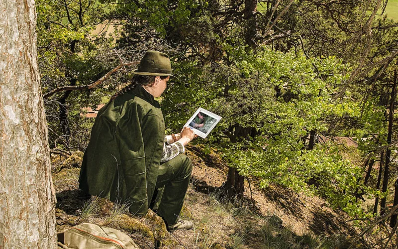Jägerin in traditioneller Kleidung nutzt ein Tablet im Wald zur digitalen Revierbeobachtung