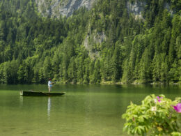 Fliegenfischer im Boot auf klarem Bergsee vor bewaldetem Felsmassiv