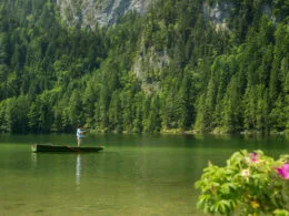 Fliegenfischer im Boot auf klarem Bergsee vor bewaldetem Felsmassiv