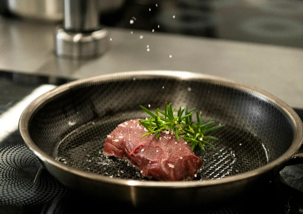 Wildfleischstück mit Rosmarin in der Pfanne beim Anbraten