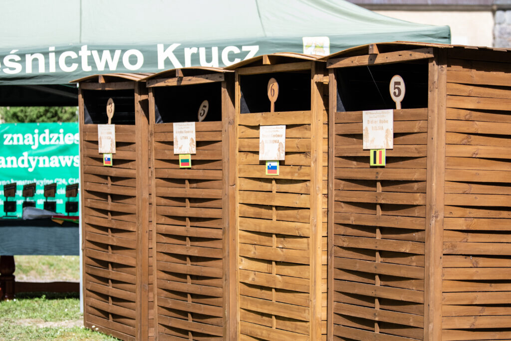Drei Sichtschutzkabinen aus Holz mit Flaggen und Namensschildern der Juroren bei der Hirschruf-Europameisterschaft 2024.