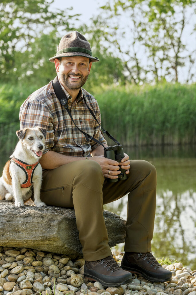 DI Christoph Metzker mit Hund und Fernglas am Ufer